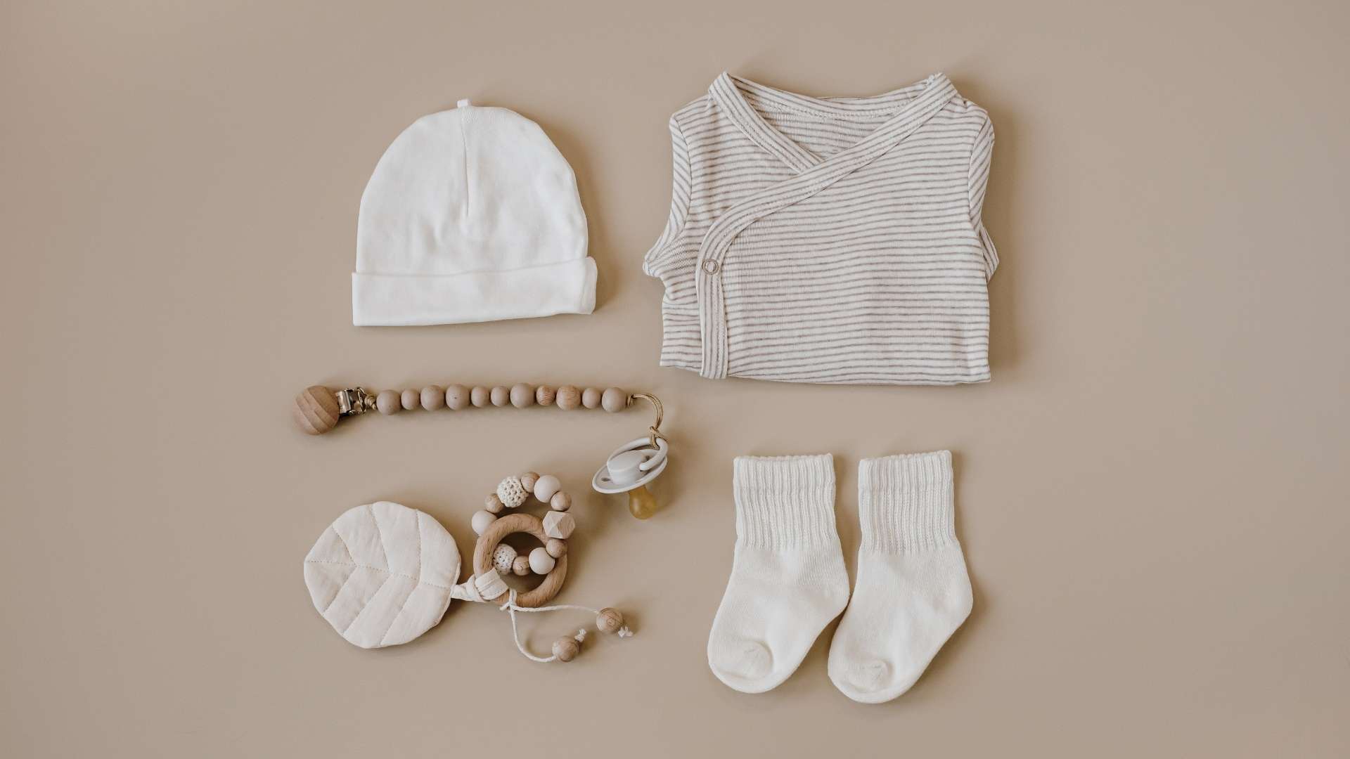 Neutral-colored baby clothes arranged on a brown background - Kuluki Fashion Marketing.